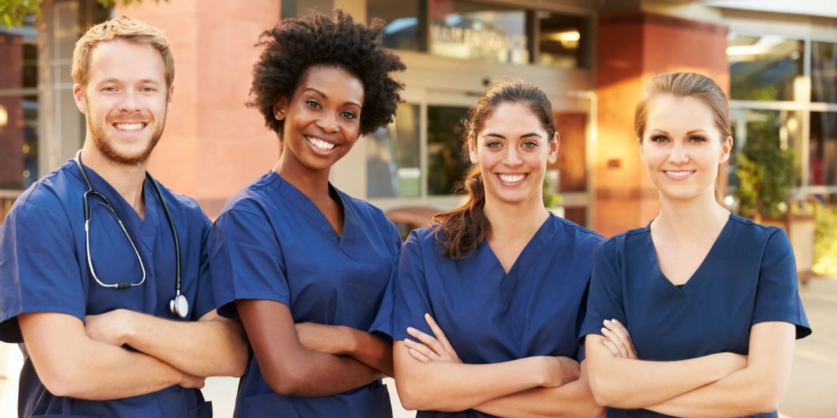 Four diverse nurses in light blue scrubs reviewing a patient chart together