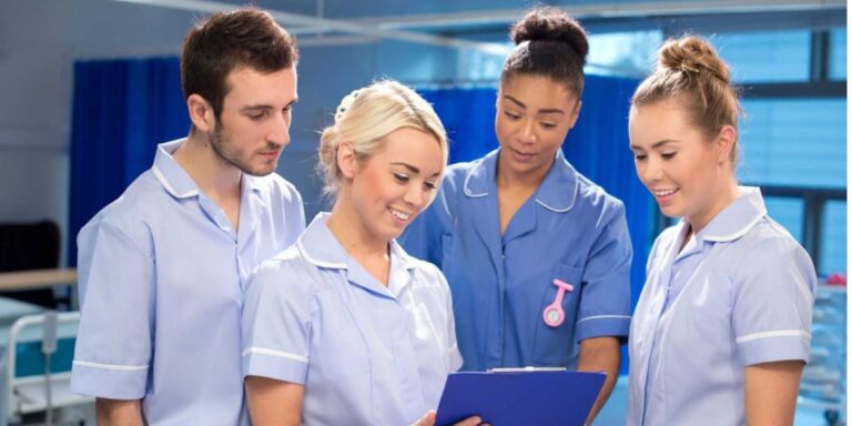 Four diverse nurses in light blue scrubs reviewing a patient chart together