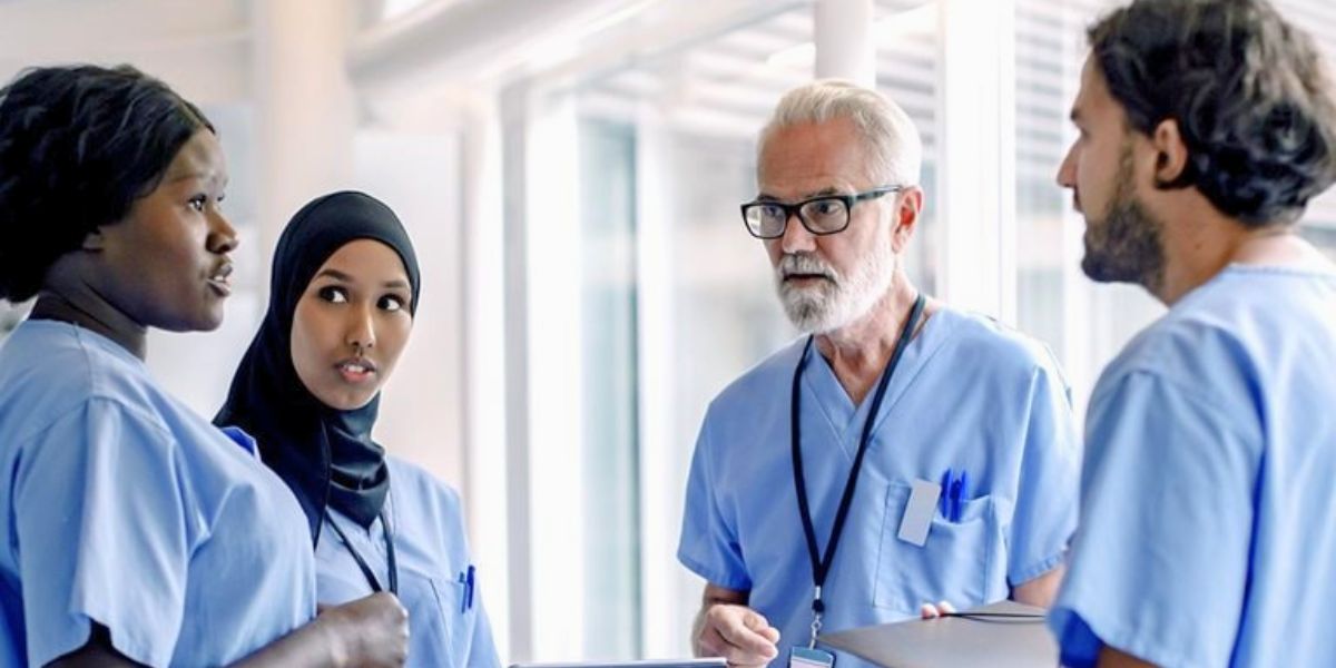 Four diverse medical staff (three women, one man) in blue scrubs discussing work.